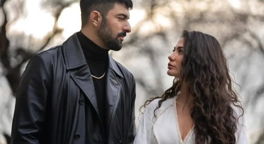 Un uomo con trench di pelle nera e una donna con lunghi capelli scuri si guardano intensamente. Io sono Farah, e questo sguardo dice tutto.