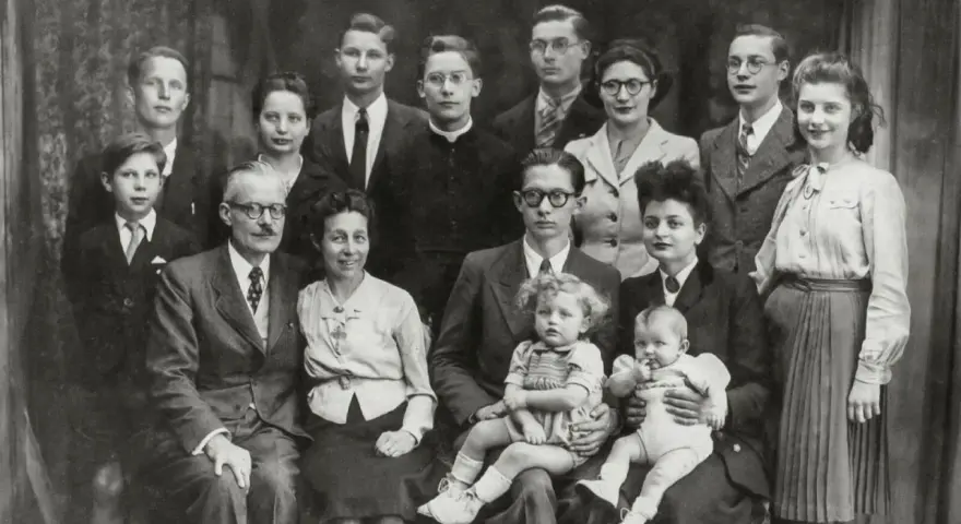 Gros plan sur une famille nombreuse posant pour une photo. On peut y voir des enfants, des adultes et des bébés. Une recherche sur Geneanet pourrait révéler leur nom de famille.