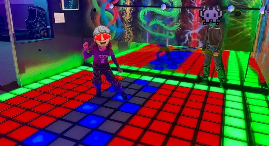 Kinder spielen im **underground lasergame Berlin** auf einer leuchtenden Tanzfläche. Bunte Drachen zieren die Wand.