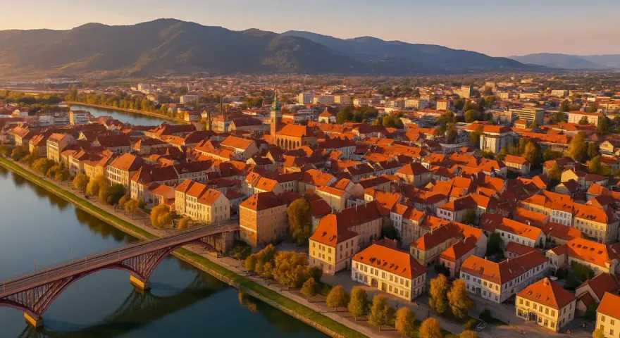 Widok na Maribor z lotu ptaka: rzeka Drava, most, zabytkowe kamienice z czerwonymi dachami i wzgórza w tle. Odkryj mariborskie atrakcje!