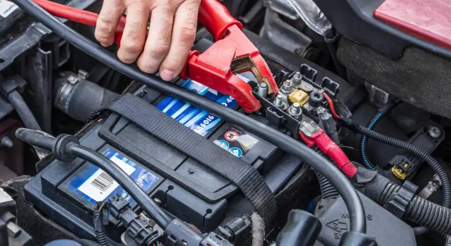 Starthilfe war zuerst: Eine Hand befestigt eine rote Klemme an der Autobatterie, um dem Fahrzeug wieder Leben einzuhauchen.