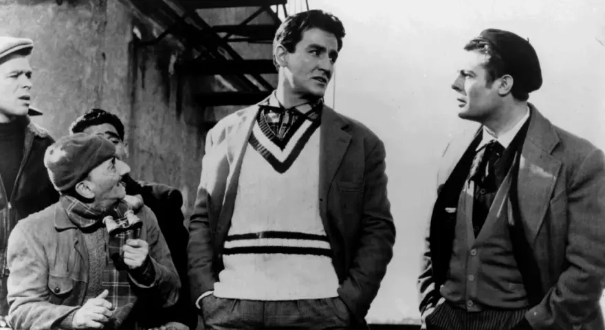 Uomini in abiti d'epoca, uno con un maglione a V, discutono animatamente. Un'iconica scena della commedia all'italiana.