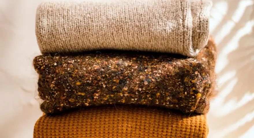 Gestapelte Strickwaren in warmen Herbstfarben. Damit die **Wolle bei 40 Grad waschen** gelingt, sind diese Pullover perfekt.