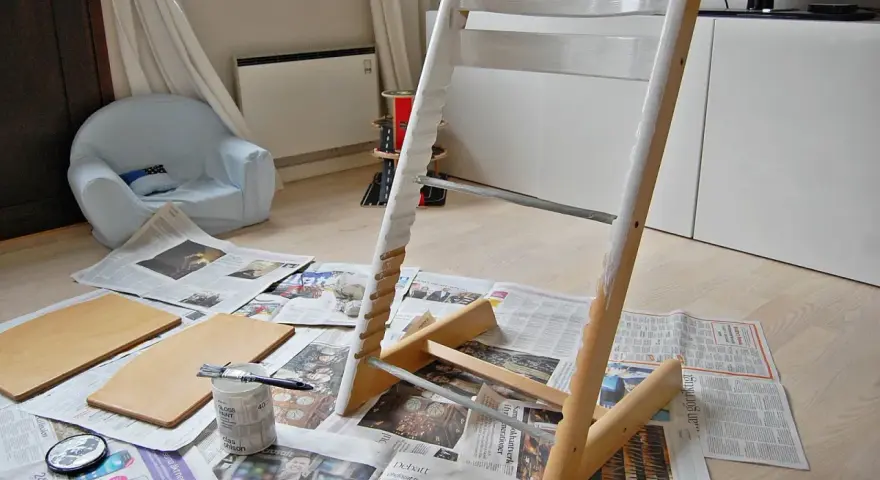 Måla om Stokke stol med vit färg. Trädelar och pensel ligger på tidningspapper.