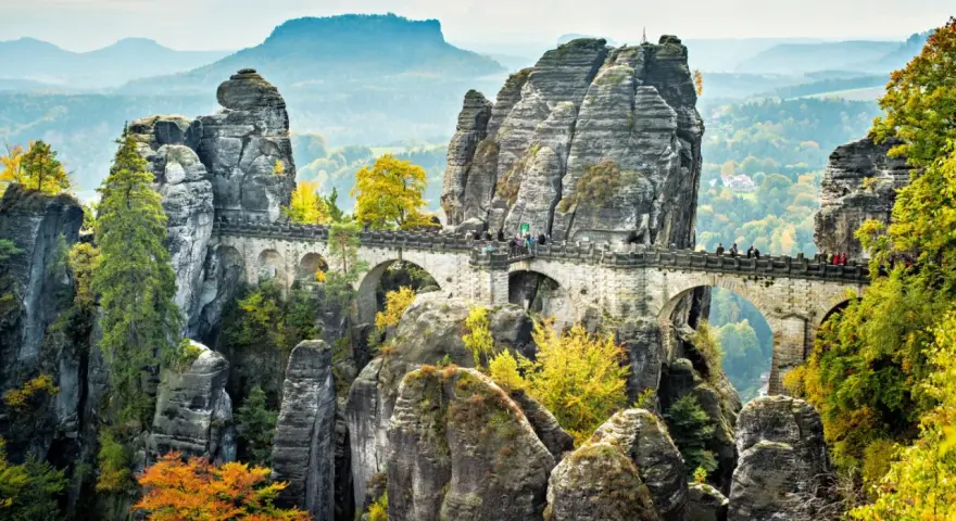 Most Bastei, skalne miasto w Saksonii, z kamiennym mostem łączącym skalne iglice. Jesienne liście dodają koloru krajobrazowi.