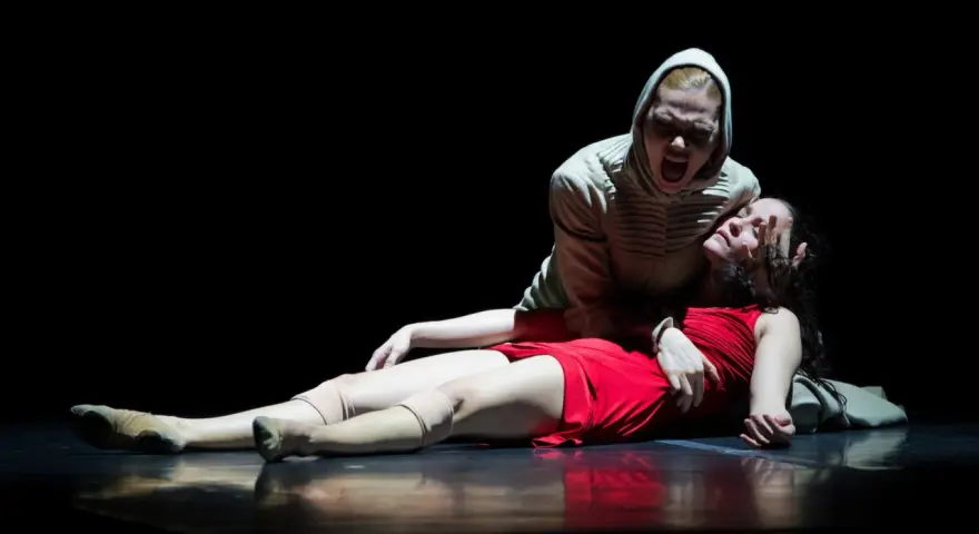 Una escena dramática de "Romeo y Julieta resumen corto": una mujer con capucha grita sobre otra, vestida de rojo, que yace en el suelo.