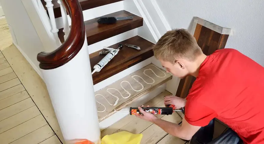 Man lägger lim på en trappsteg för att lägga nytt golv. Trappa inomhus inspiration för ett modernt hem.