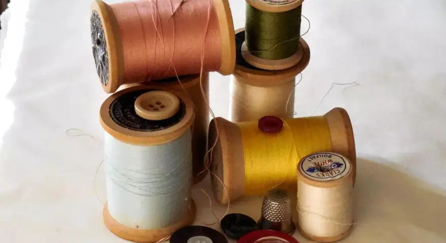 Bobine di filo colorato, bottoni e un ditale, pronti per un punto sopraggitto a mano.