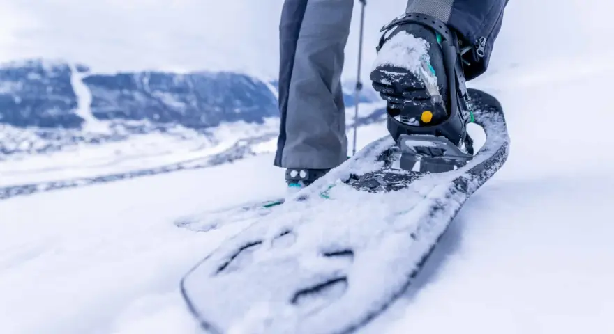 Piede con racchette da neve che affonda nella neve fresca, pronto per camminare in montagna.