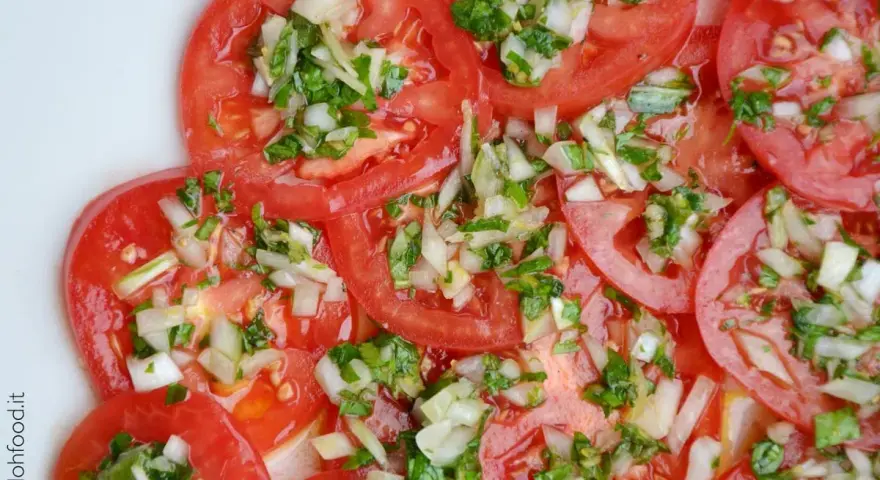 Fette di pomodoro fresco condite con cipolla tritata e erbe aromatiche. Un'insalata di pomodori semplice e gustosa.