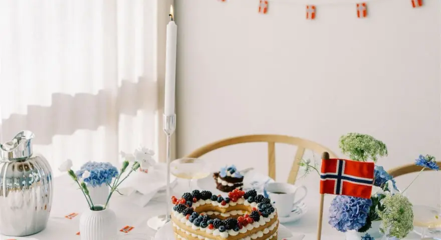 Festligt dukat bord med hjärtformad tårta, blommor och norska flaggor. Perfekt för firande med flaggor att skriva ut.
