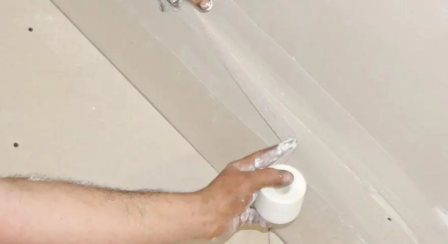 Hände arbeiten an einer q4 Spachtelung. Eine Rolle Klebeband wird gehalten, während die andere Hand die Spachtelmasse aufträgt.