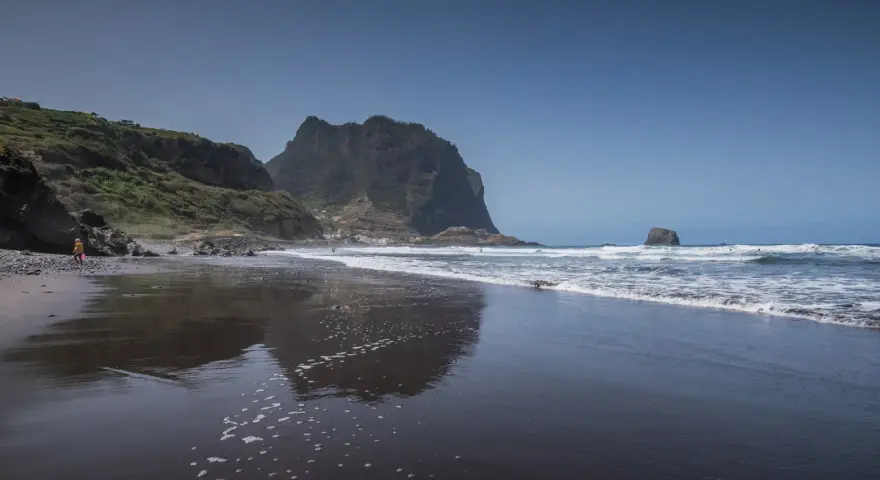 Dziecko bawi się na czarnej plaży Madera, w tle widać skaliste klify i ocean.