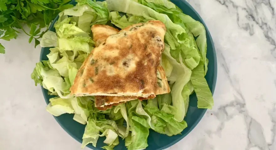 Puszysty omlet z ziołami na talerzu z sałatą.