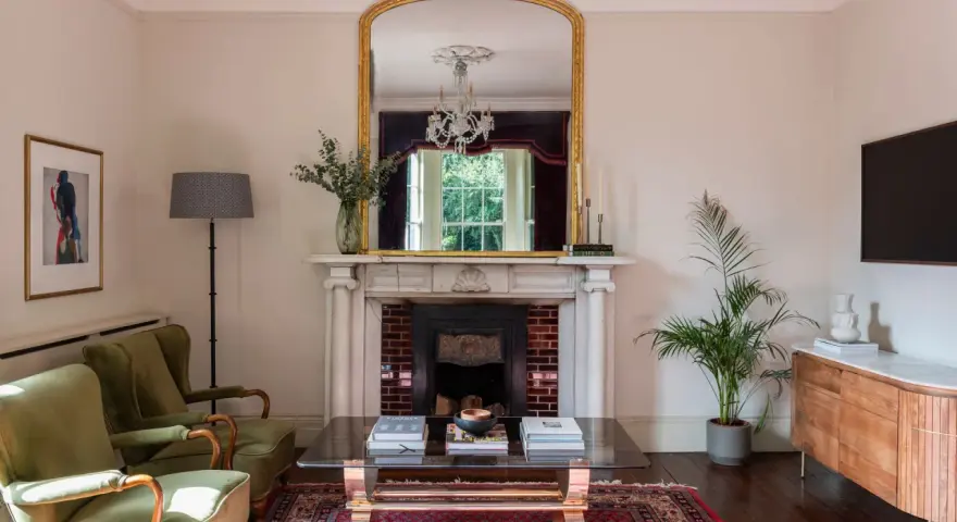 Sofá verde, chimenea con espejo dorado y candelabros. La sala de estar exhibe colores elegantes y un ambiente acogedor.