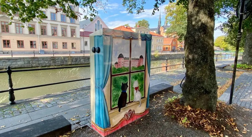 En målad låda med två katter som tittar ut genom ett fönster på ett slott. Konstnären har valt att måla tunt för att ge en drömsk känsla.