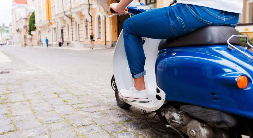 Un uomo in jeans guida uno scooter blu su un lastricato, un'immagine che evoca la libertà e lo spirito dell'art 52 cds.