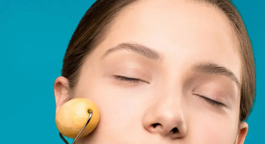 Mujer con ojos cerrados disfrutando de un masaje facial antienvejecimiento y drenaje con rodillo de jade.