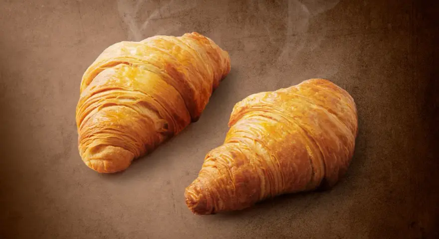 Dwa złociste croissanty z nadzieniem orzechowym z Lidla, parujące delikatnie. Idealne na śniadanie, zaspokoją głód i dostarczą energii.