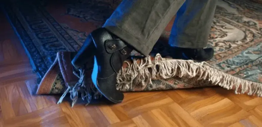 En fot med klacksko snubblar på en matta. En antiglidmatta hade kunnat förhindra detta.