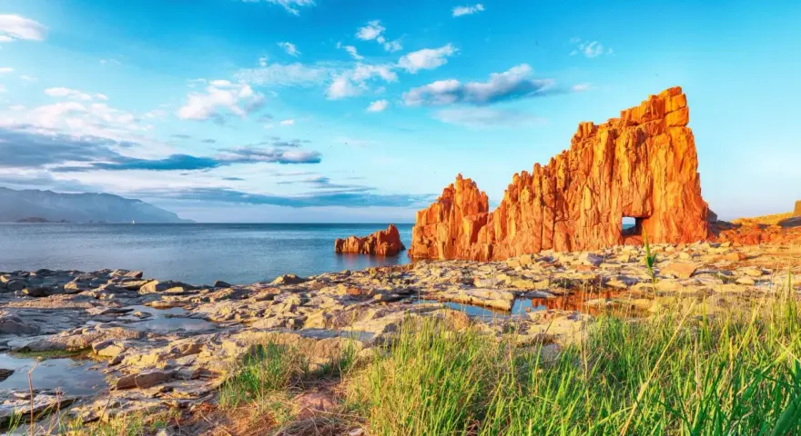 Scogliere rosse a picco sul mare blu, con un arco naturale, vicino ad Arbatax centro storico.