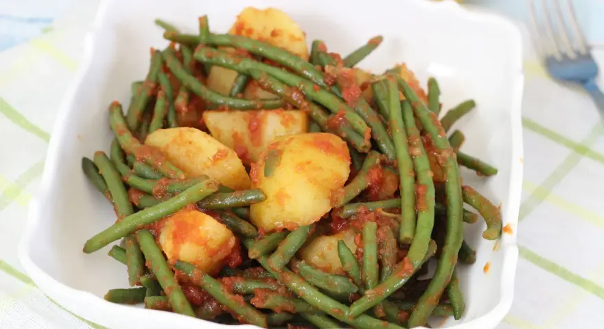 Fagiolini in umido con patate, un piatto saporito e colorato, servito in una ciotola bianca su una tovaglia a quadri.