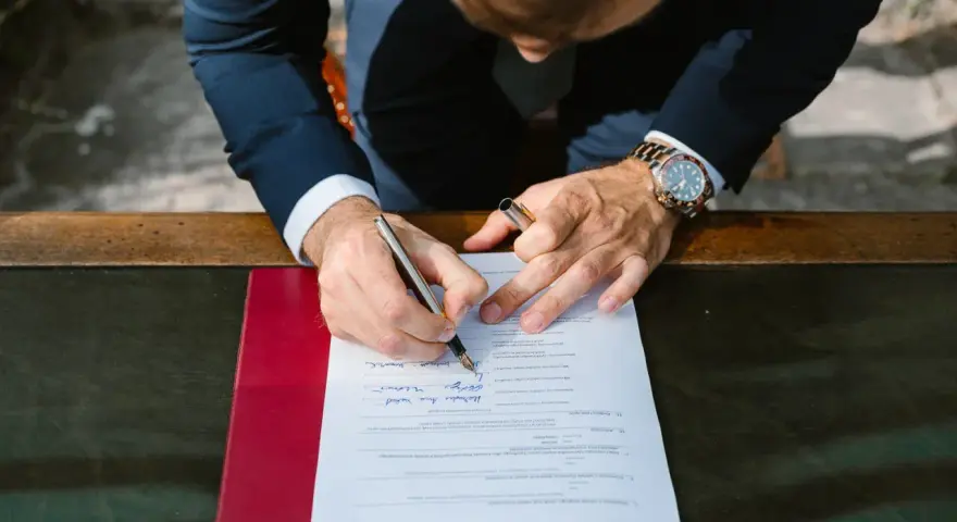 Mężczyzna w garniturze podpisuje dokument. Zastanawia się, jakim nazwiskiem podpisać się na ślubie cywilnym, wybierając to właściwe.