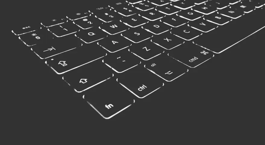 Nahaufnahme einer beleuchteten Tastatur. Die Tasten sind mit weißen Symbolen und Buchstaben versehen, die im Dunkeln leuchten. Die "Umschalt"-Taste ist deutlich zu erkennen.