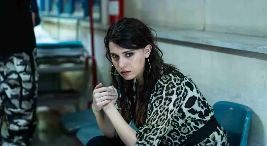 Carmela, con sguardo intenso, attende il suo destino fuori dal carcere. Indossa una camicia leopardata.