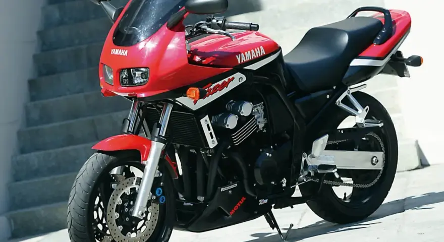 Czerwony motocykl Yamaha FZ6 z czarnym siedzeniem i owiewką, zaparkowany na zewnątrz.