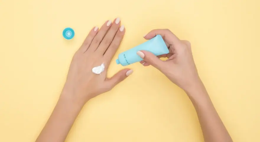 Hände mit Creme, die Glycerin enthält, auf gelbem Hintergrund.