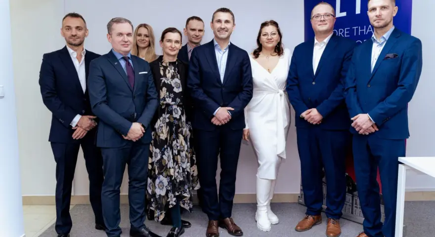 Grupa osób w garniturach i sukience pozuje do zdjęcia na tle banera.