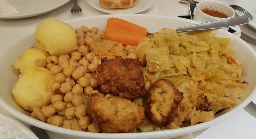 Un plato generoso de cocido madrileño con garbanzos, patatas, zanahoria, repollo y trozos de carne frita.