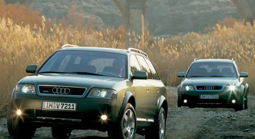 Dwa Audi A6 C5 2.5 TDI Allroad jadące po kamienistej drodze, w tle łuk mostu i suche trawy.