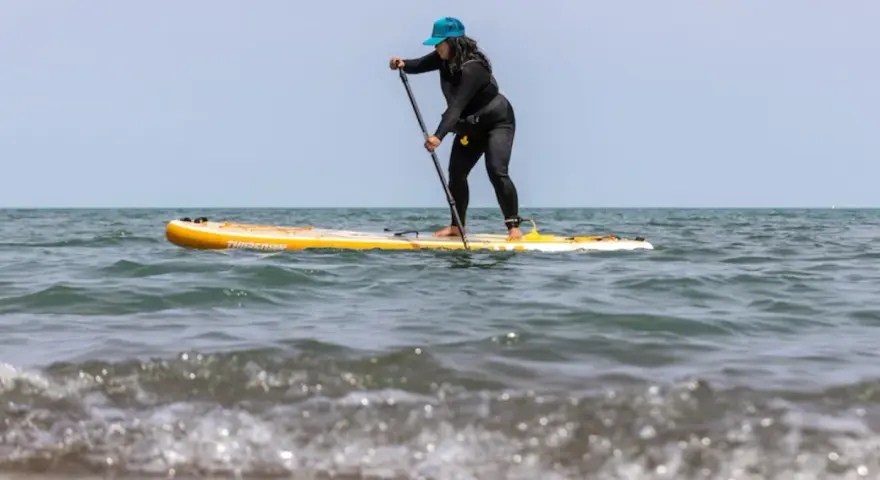 Frau auf einem gelben Stand Up Paddle Board im Meer, mit Paddel in der Hand.