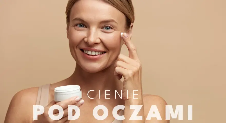 Uśmiechnięta kobieta aplikuje krem pod oczy. To rozwiązanie na cienie pod oczami, które przywróci blask Twojej skórze.