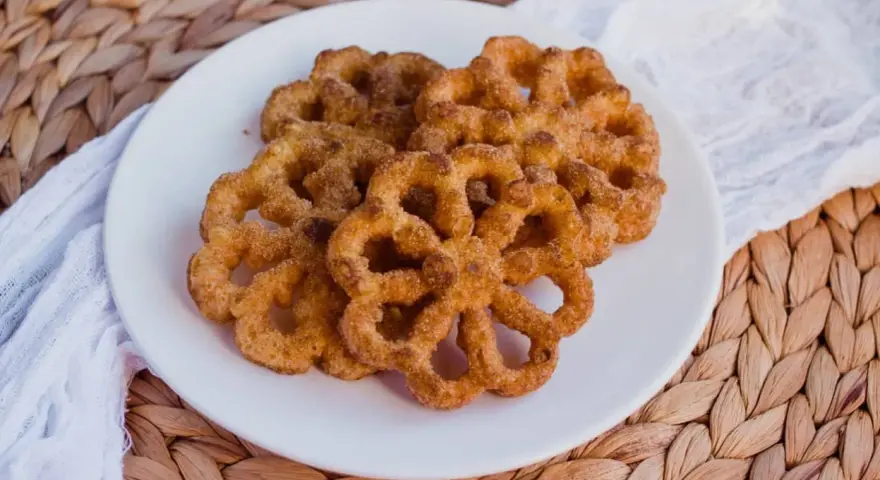 Buñuelos dorados con azúcar y canela en un plato blanco.