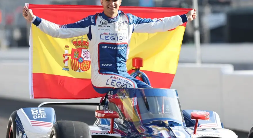 Alex Palou celebra su victoria en las 500 millas de Indianápolis, ondeando la bandera de España sobre su coche de carreras.