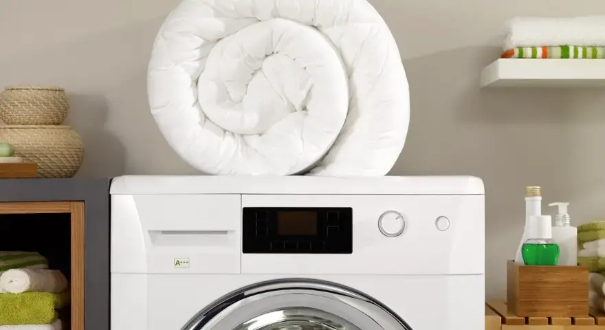Piumone bianco arrotolato sopra una lavatrice. Pronto per essere lavato in lavatrice a 40 gradi per un bucato fresco e pulito.