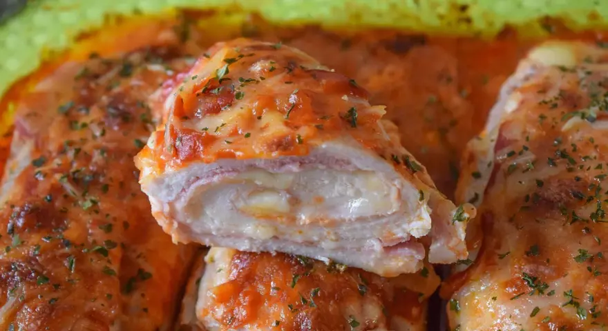 Pechugas de pollo rellenas de queso y jamón, cubiertas con salsa de tomate y queso gratinado, espolvoreadas con perejil fresco.