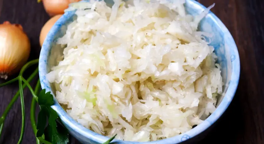 Schüssel mit weltbestem Krautsalat, daneben Zwiebeln und Petersilie. Frisch, knackig und voller Geschmack!