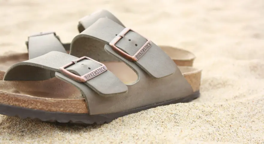 Sandali Birkenstock grigi sulla sabbia. Scopri come si lavano le Birkenstock per mantenerle perfette.