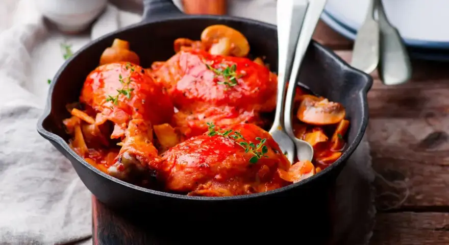 Pollo alla Marengo succulento in padella con funghi e pomodoro, guarnito con timo fresco.