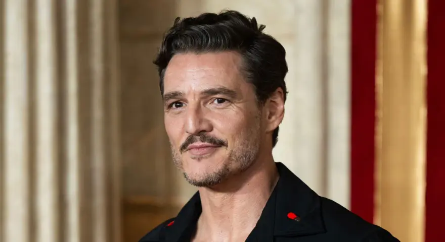 Pedro Pascal con cortes de pelo hombre corto por los lados y largo arriba, luciendo un pin de cerilla en su solapa.