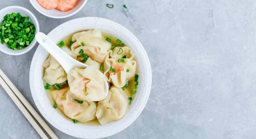 Aksamitna zupa wonton z krewetkami i szczypiorkiem, podana z pałeczkami.