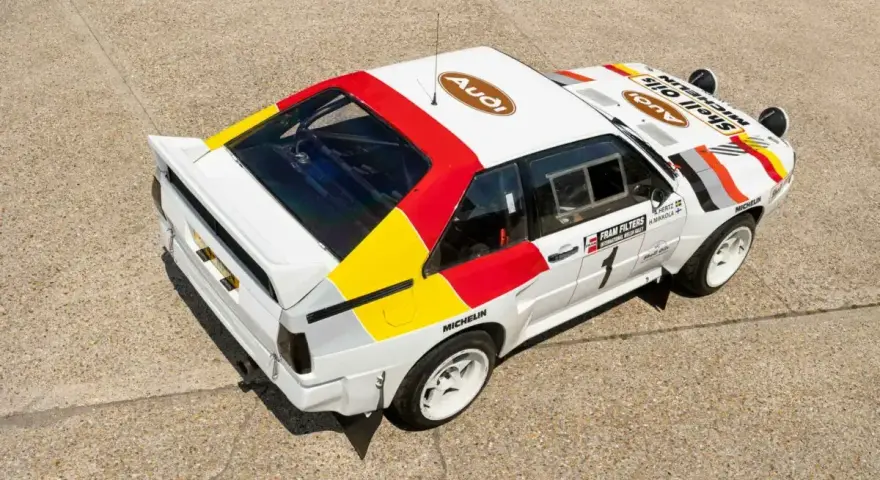 Biały rajdowy **Audi quattro S1** z kolorowymi pasami i logotypami sponsorów, gotowy do podboju szutrowych tras.