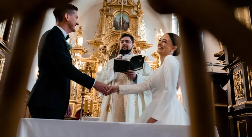 Para młoda ściska dłoń księdza podczas ceremonii. Zastanawiasz się, ile trwają nauki przedmałżeńskie?