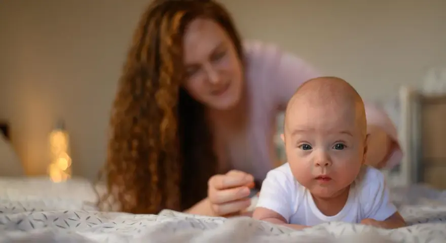 Maluch ćwiczy mięśnie szyi, kiedy układać noworodka na brzuchu. Mama czuwa z tyłu.