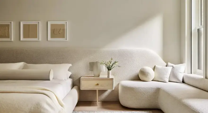 Dormitorio con decoración minimalista, cama baja, sofá curvo y arte abstracto en tonos tierra.