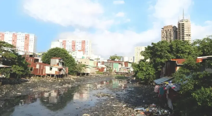 Un río lleno de basura y aguas residuales, rodeado de casas precarias y edificios modernos, ilustra los graves tipos de contaminación que afectan a esta comunidad.